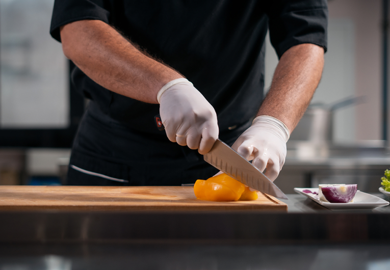 close up of chef cook hands in gloves cutting or chop yellow pepper at kitchen with knife
