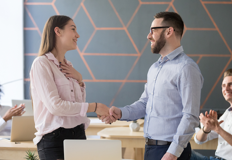 Male boss or team leader shaking hand of female successful employee congratulating with promotion or rewarding, appreciating for good work result while business team applauding.