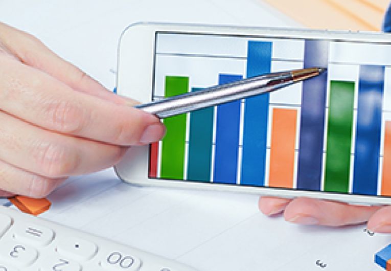 Business professional showing a bar chart through a mobile phone at a desk.