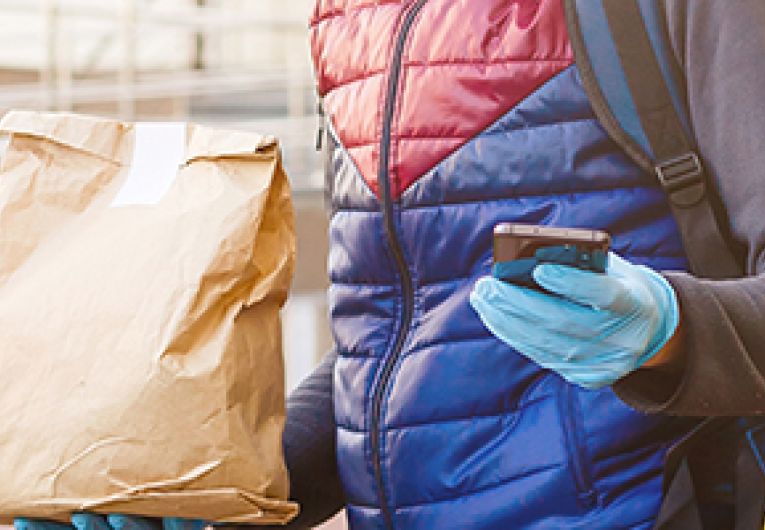Delivery person looking at a mobile device while holding a large brown bag.