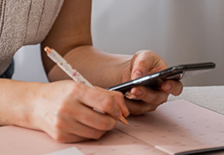 A business professional holds a smartphone while taking notes.