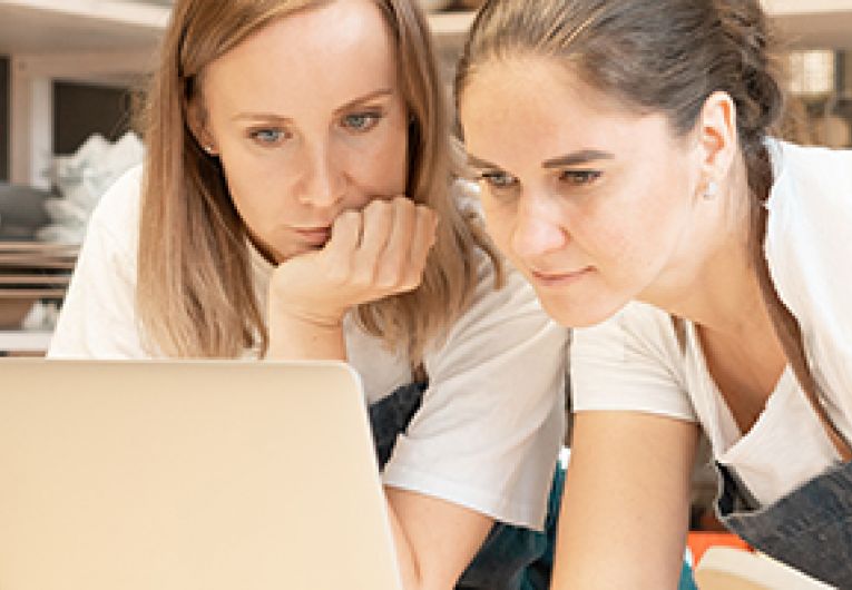 Two women entrepreneurs look at a laptop screen together.