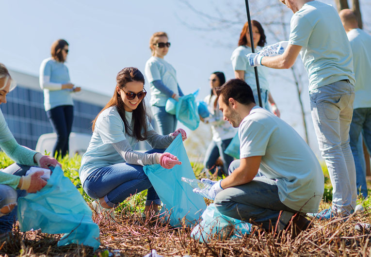 volunteering, charity, cleaning, people and ecology concept - group of happy volunteers with garbage bags cleaning area in park