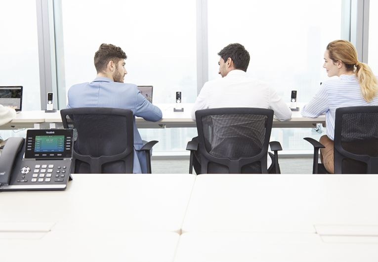 Business professionals sitting in conference room with desktop phone sitting on table. 
