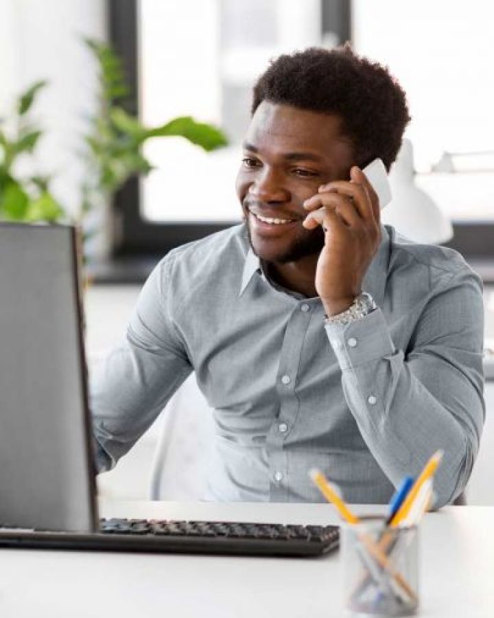 Man sitting in office talking on a cellphone and looking at a laptop