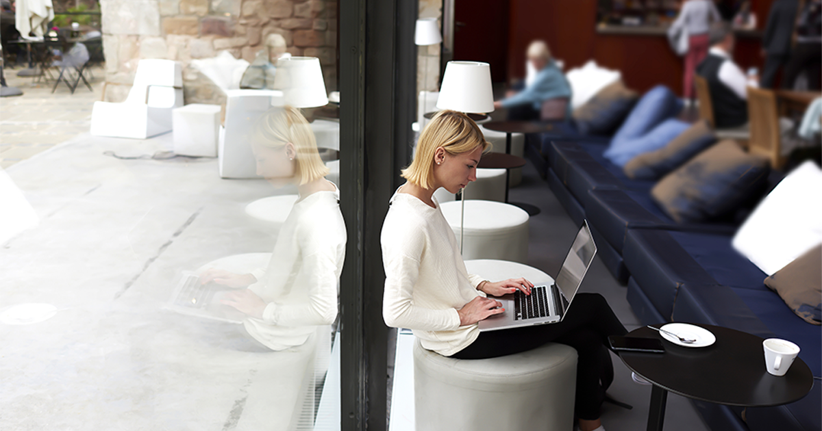 Female student connecting to wireless via laptop computer while sitting in modern coffee shop or university library