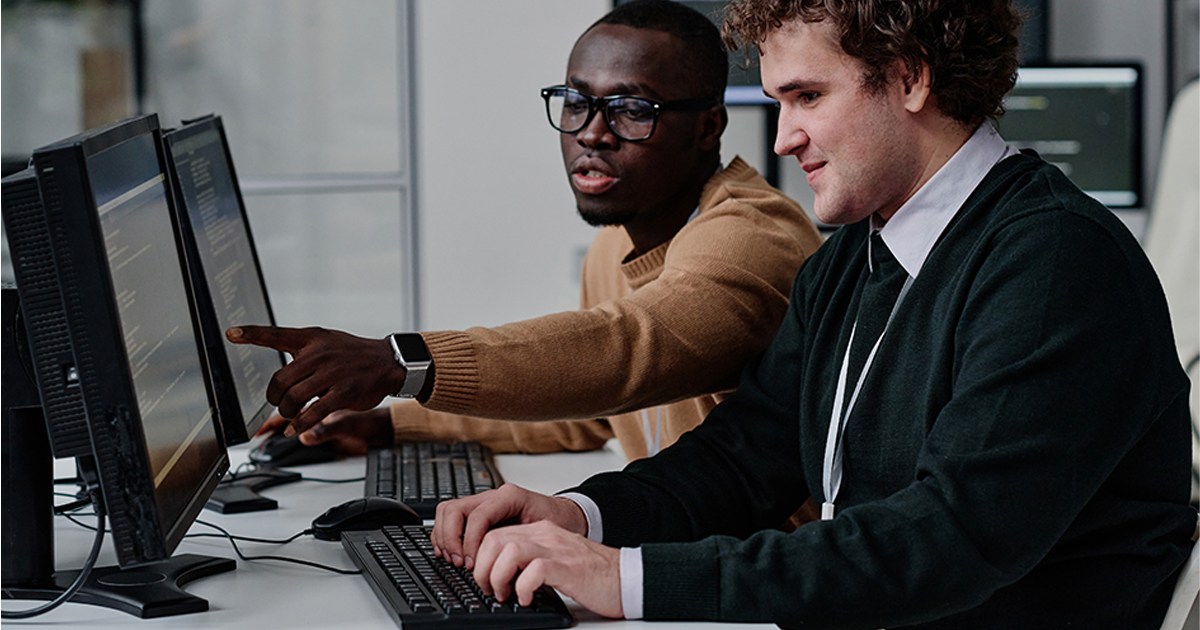 Programmer pointing at computer monitor with codes and talking to his colleague while they working with computer program in team
