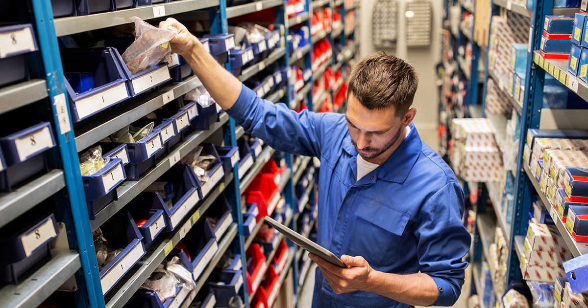 Auto mechanic with tablet computer looking for parts at workshop or warehouse.