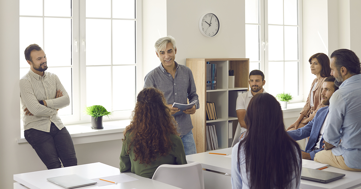 Team of people listening to senior business coach during training meeting in office