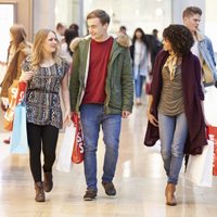 three people with shopping bags walking through a mall