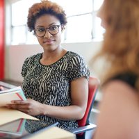 A woman sitting in a desk listening to her peer.