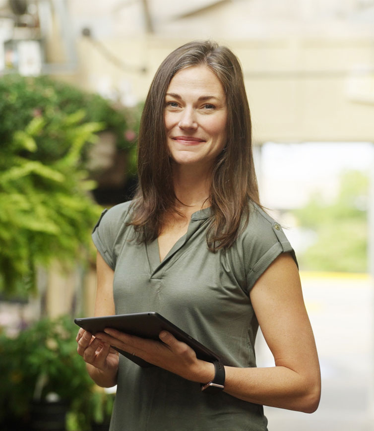 Woman working in a garden nursery smiling and holding a tablet