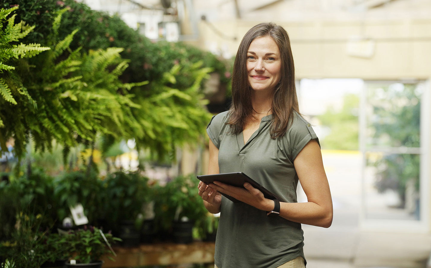 Woman working in a garden nursery smiling and holding a tablet
