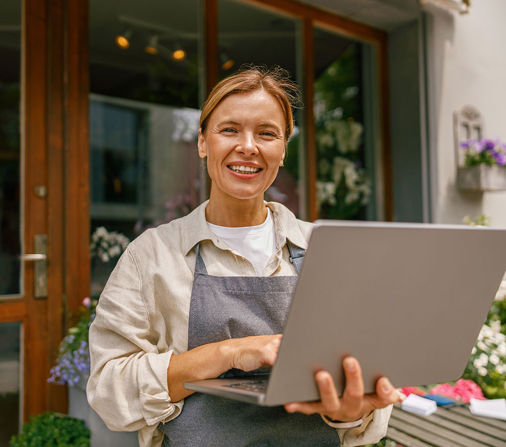 Woman wearing a work apron smiling and holding a tablet outside a business